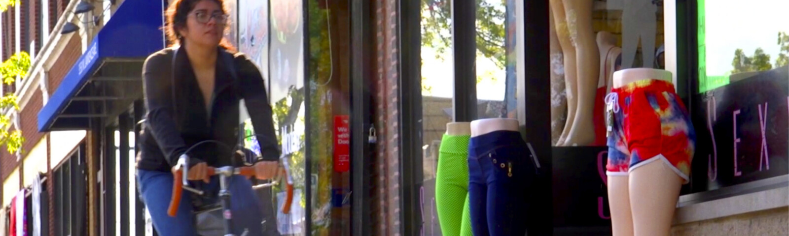 A person riding a bicycle past a clothing store on an Albany Park street